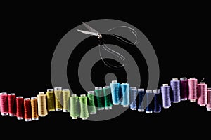 Top view of bright and colorful threads and scissors isolated on black.