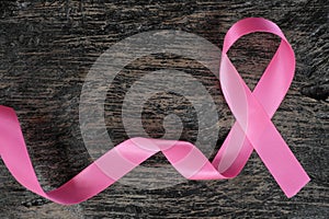 Top view of bright pink ribbon on dark wood background. Breast cancer awareness and women`s health concept.