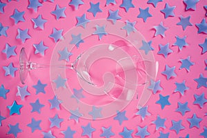 Top view of broken champagne glass with splinters and pattern of blue stars sequins on pink background. Wineglass fallen