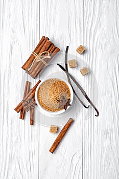 Top view of brown cinnamon granulated and cane cubes sugar with spices on white wooden background