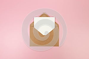 Top view of brown kraft envelope, white card on pink background.