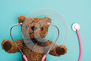 Top view of brown teddy bear with pink stethoscope on blue background, international childhood cancer day concept. photo