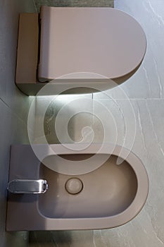 Top view of brown toilet and bidet. Modern wc interior. Gray floor and wall of the bathroom. Bottom light. Home interior design