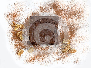 Top view of a brownie surrounded with sprinkled cocoa and walnuts
