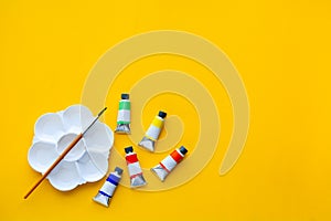 Top view of brushes, color tubes and palette on yellow background, copy space, flat lay, paintings art concept