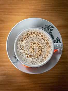 Top view of bubbles on the white coffee served in Kopitiam cup on the wooden table