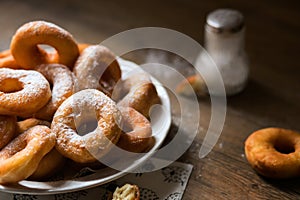 Top view on a bunch of fresh homemade donuts (doughnuts) on a white plate, with sugar bowl, rolling pin