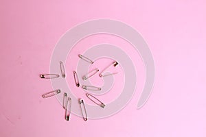 Top view of a bunch of safety pins on a pink background