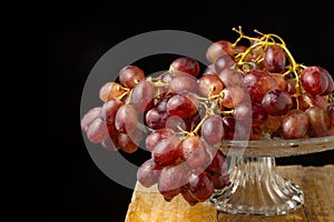 Top view of bunch of wet red grapes on glass cake stand on wooden table, selective focus, black background