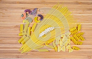 Uncooked various pasta and wheat ears on the wooden surface