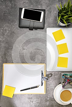 Top view of business desk with laptop, mobile phone, coffee, potted plant, notebook, notes paper, clipboard and business