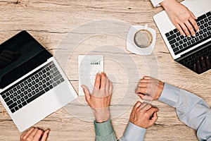 Top view of business people using laptops and calculator by coffee on table