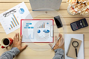 Top view business person discussing charts and graphs also notebook,black coffee,flower,stationary,pen,calculator on office desk