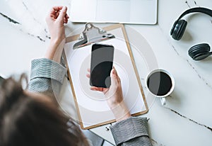 Top view of business woman on working place with cup of coffee, notes, open laptop, smartphone on white marble table in the bright