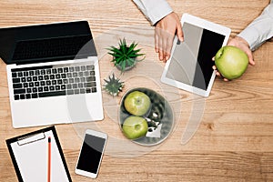 Top view of businessman holding apple beside digital tablet, laptop and smartphone