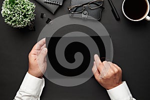 Top view of businessman`s hands working with tablet pc. Modern black office desk with notebook, pen and a lot of things. Flat lay