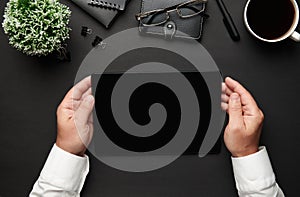 Top view of businessman`s hands working with tablet pc. Modern black office desk with notebook, pen and a lot of things. Flat lay