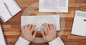 Top view of businessman typing on wireless keyboard with notepad pen calculator and financial report concept