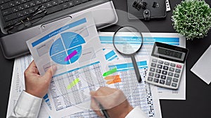 Top view of businessman working with financial statements. Modern black office desk with notebook, calc, pen and a lot of things.