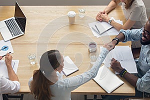 Top view businesswoman handshaking African American partner at group meeting