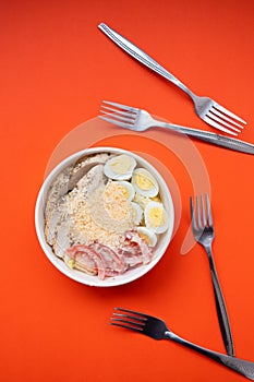 Top view of Caesar salad with lettuce, tomatoes, eggs, croutons, chicken and sauce in paper bowl