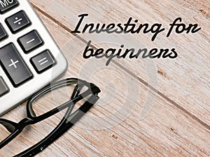 Top view calculator and eye glasses with text Investing for beginners written on wooden background.