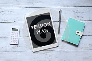 Top view of calculator,notebook,pen and tablet pc written with 'PENSION PLAN' on wooden background