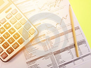 Top view of calculator, pencil and company summary data charts on yellow background