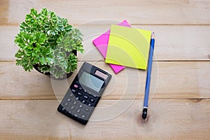 top view calculator,post it note,pencil and some plant put on wooden