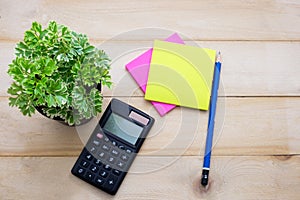 top view calculator,post it note,pencil and some plant put on wooden