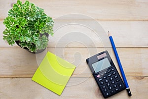 top view calculator,post it note,pencil and some plant put on wooden