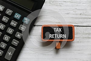 Top view of calculator and red tag written with TAX RETURN on white wooden background