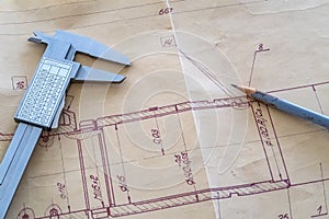 Top view of a caliper measuring tool and pencil on a drawing.