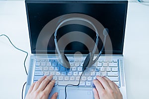 Top view of the call center operator`s desktop. Close-up of female hands typing on a laptop. Unrecognizable woman works