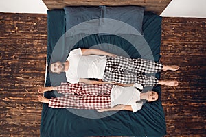 Top view. Calm young couple lies across bed perpendicular to each other.
