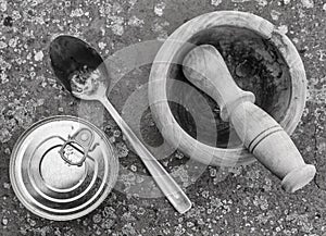 Top view of a can of packaged food, a wooden mortar and a metal spoon on a spotted background, in black and white