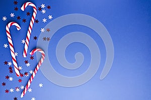 Top view of candy canes, confetti on the blue background, empty space for text