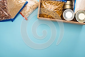 Top view of cans and groats in zipper bags in wooden box on blue background