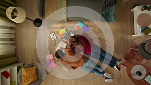 Top view capturing a young couple laying on the floor next to each other and studying, working on a laptop and taking