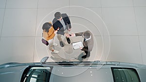 Top view of car buyers shaking hands with dealer hugging indoors in dealership