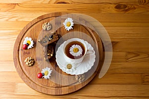 Top view of carrot cakes in a section with walnuts and spices,a white porcelain Cup with a saucer and tea, walnuts, daisies with