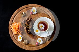 Top view of carrot cakes in a section with walnuts and spices,a white porcelain Cup of tea, walnuts, daisies with ladybirds and