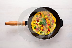 Top view of a cast iron frying pan with scrambled eggs, tomatoes and greens on a white background