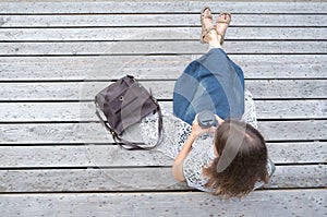 Top view casual wearing woman with trendy leather bag sitting on wooden bench in the park and drinking hot coffee on-the-go.