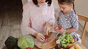 Top view of caucasian family, mother and daughter enjoy cooking salad together in kitchen