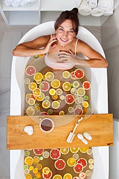 Top view of caucasian female in swimsuit sitting in bathtub with fresh slices of tropical fruits.