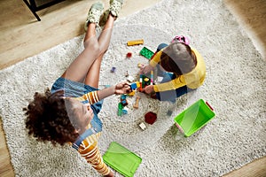 Top view of caucasian little girl spending time with african american baby sitter, playing with construction toys set