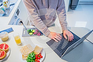 Top view caucasian male hands cooking vegetarian lunch on the kitchen table and working on pc laptop. Work from home. Home office