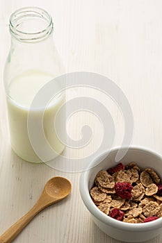 Top view of cereal bowl, milk bottle and wooden spoon, on white wooden table, in vertical