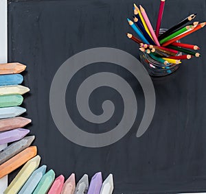 Top view of chalkboard with chalk and colored pencils